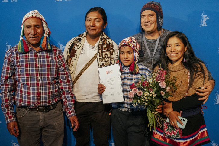 Schauspieler in traditioneller peruanischer bunter Kleidung. In der Mitte steht ein junge, der einen Preis der Berlinale in der Hand hält. 