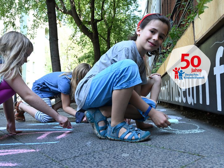 Kinder malen mit Kreide auf eine Straße. 