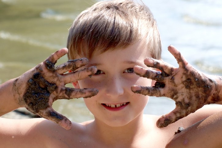 Ein Junge fährt sich fröhlich mit seinen Händen durch sein matschbeschmiertes Gesicht. 