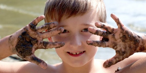 Ein Junge fährt sich fröhlich mit seinen Händen durch sein matschbeschmiertes Gesicht. 