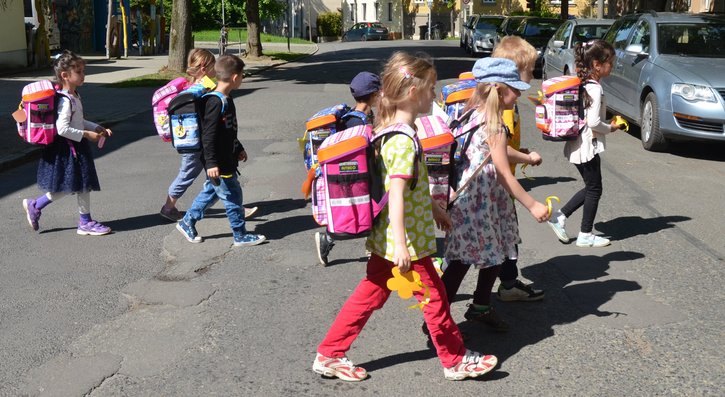 Kinder, die Schulranzen tragen, überqueren eine Straße. 