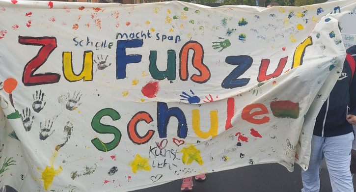 Auf einem Banner steht in bunten Farben "Zu Fuß zur Schule" 