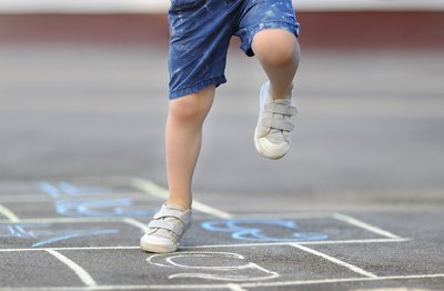 Ein Kind springt durch ein mit Kreide aufgemaltes Kästchenspiel. 