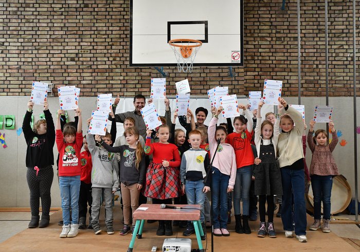Eine Gruppe von Kindern hält in einer Turnhalle stolz ihre Urkunden zur Kinderrechteschule hoch.