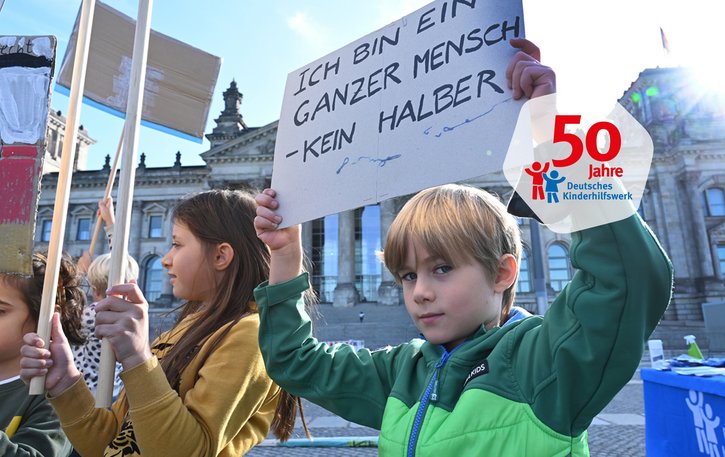 Ein Junge hält bei einer Demonstration für Kinderrechte vor dem Reichstag ein Schild hoch, auf dem "Ich bin ein ganzer Mensch, kein halber" steht, 