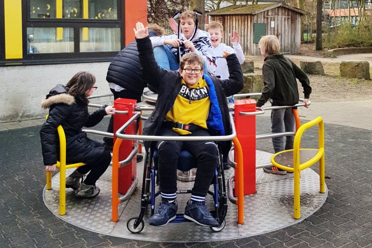 Kinder mit und ohne Behinderung fahren auf einem Rollstuhlkarussell. 