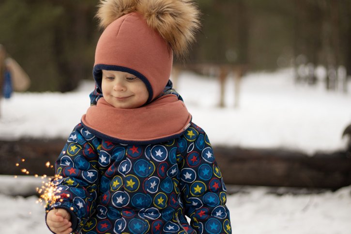 Ein Mädchen steht im Schneeanzug im Wald und hält eine Wunderkerze in der Hand. 