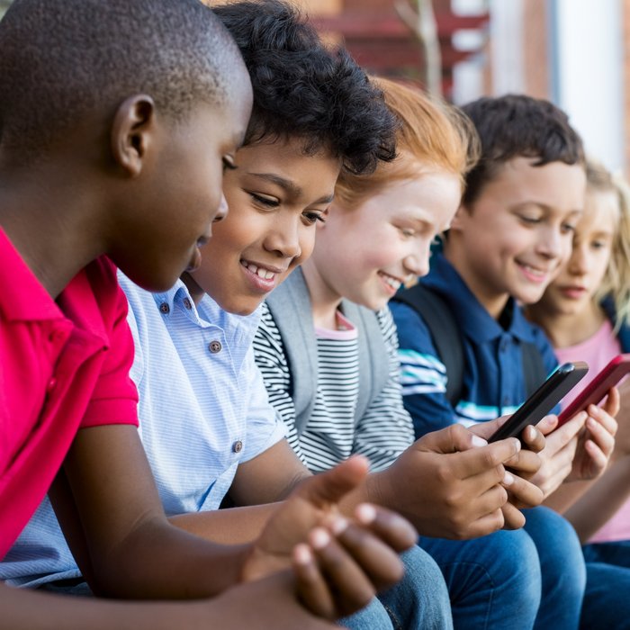 Eine Gruppe von fünf Kindern unterschiedlichen Geschlechts und Ethnien sitzt nebeneinander und schaut auf ihre Smartphones.