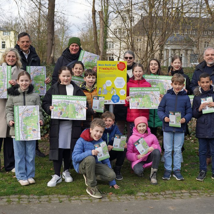 Kinder und Erwachsene stehen im Kurpark Unna vor einem neu eröffneten Schild, auf dem Lehrpfad der Kinderrechte steht.
