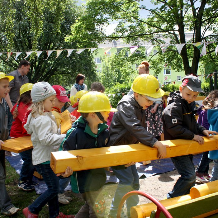 Kinder tragen gelbe Bauhelme und stecken Holzteile zusammen. 