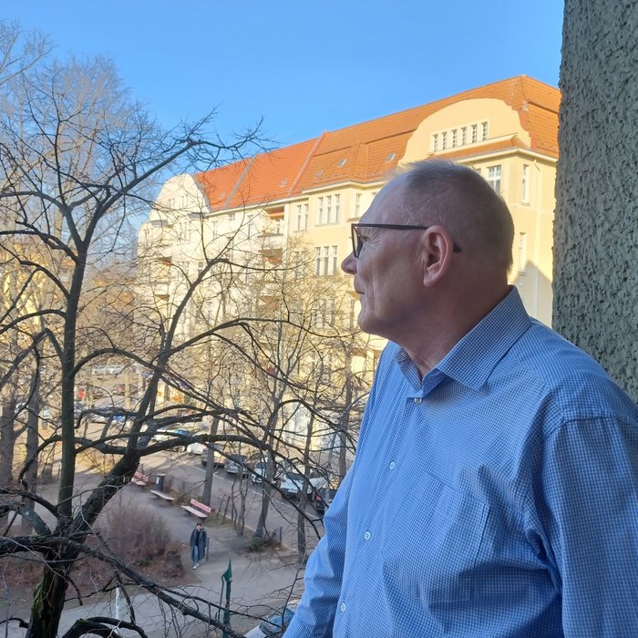 Ein ältere Mann schaut von seinem Balkon aus in die Ferne.