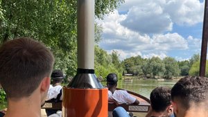 Die Jugendlichen sitzen in einem Boot und fahren über einen Fluss. Man sieht nur die Hinterköpfe.