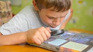 Junge prüft Text mit einer Lupe