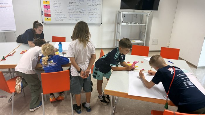 Die Kinder sind um Tische versammelt und arbeiten an ihrem Kinder- und Jugendbeteiligungsgremium.