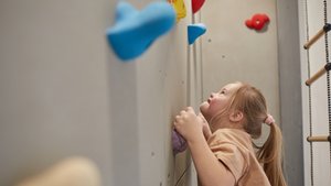 Ein Mädchen klettert an einer Wand mit bunten Klettergriffen. 