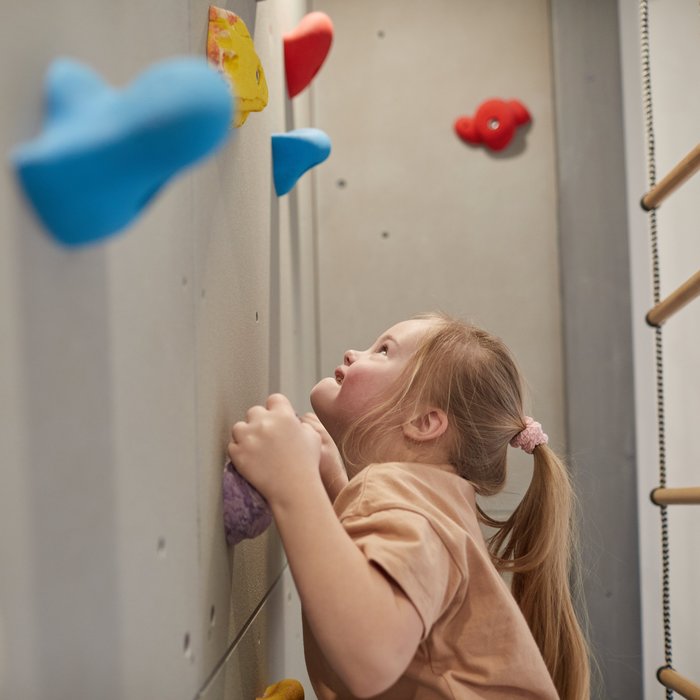 Ein Mädchen klettert an einer Wand mit bunten Klettergriffen. 