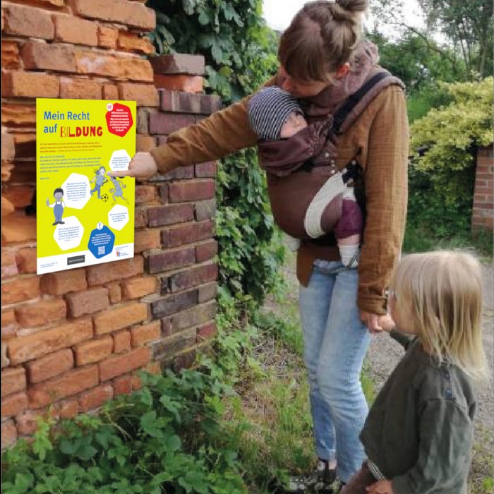 Eine Mutter schaut mit ihren 2 kleinen Kindern ein Schild des Deutschen Kinderhilfswerkes zum Thema Lernpfad an.