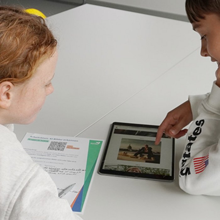 Ein Junge und ein Mädchen in weißen Pullovern schauen gemeinsam in ein Tablet. 