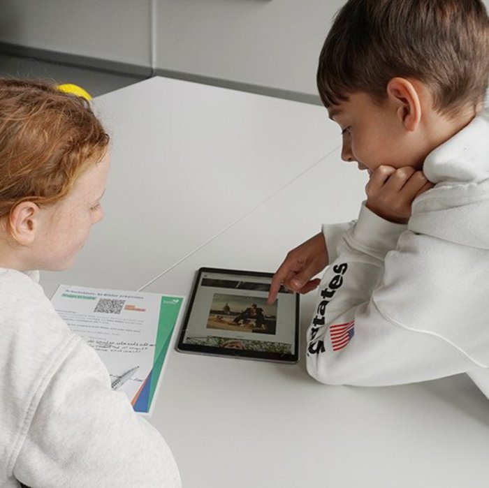 Ein Junge und ein Mädchen in weißen Pullovern schauen gemeinsam in ein Tablet. 