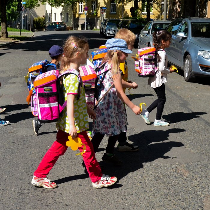 Mehrere Kinder mit Schulranzen überqueren gemeinsam eine Straße. 